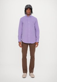 Cămașă mov cu guler, pantaloni maro și o șapcă închisă. Cămașa are o textură subtilă, iar pantalonii sunt drepți.