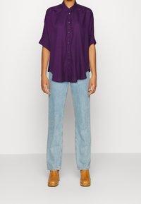 Lila kortärmad skjorta med knappar och avslappnad passform, ihop med ljusblå raka jeans och bruna ankelboots.