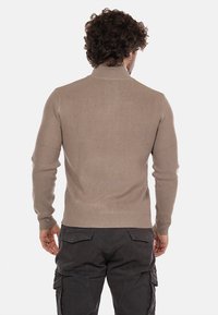 Maglione lavorato a maglia beige con colletto alto e texture a costine. Design aderente, maniche lunghe e finitura liscia sul retro.