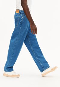 Lichtblauwe denim jeans met een rechte pijp, voorzien van achterzakken en een bruine leren patch. Gestyled met witte en beige sneakers.