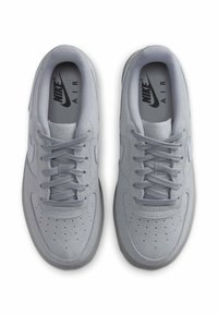 Světlé šedé tenisky Nike Air s semišovou texturou, perforovaným svrškem, plochými tkaničkami a jemným logem na stélce a boku.
