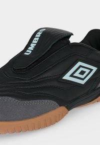Μαύρο και γκρι αθλητικό παπούτσι Umbro με λάστιχο σόλα, με κλειστό σύστημα κορδονιών και το λογότυπο Umbro στο πλάι και στο καπάκι.