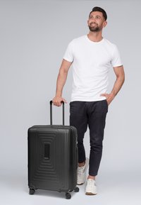 Maleta negra con diseño estriado, mango retráctil, cuatro ruedas giratorias y un asa central. Superficie texturizada y forma elegante.