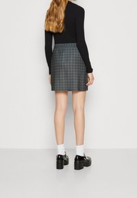 Rutig minikjol i mörkgrått och svart med elastisk midja, kombinerad med svarta klumpiga skor och vita strumpor. Långärmad svart topp.