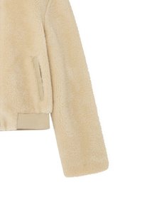 Chaqueta de piel sintética beige con textura suave, puños acanalados y un bolsillo lateral. Diseño informal con un corte cropped y líneas limpias.
