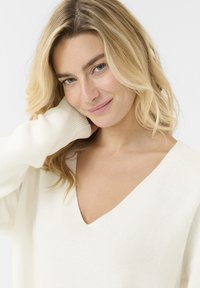 Elfenbeinfarbener V-Ausschnitt-Pullover mit strukturiertem Strickmuster, langen Ärmeln und lässiger Passform. Weicher Stoff liegt bequem am Hals an.