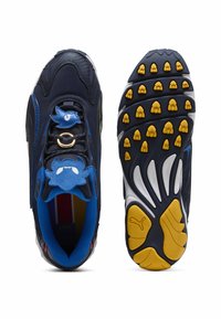 Sneaker blu navy con accenti blu e giallo, caratterizzato da dettagli cartoon, un charm a forma di uccello sui lacci e una suola testurizzata con motivi di presa gialli.