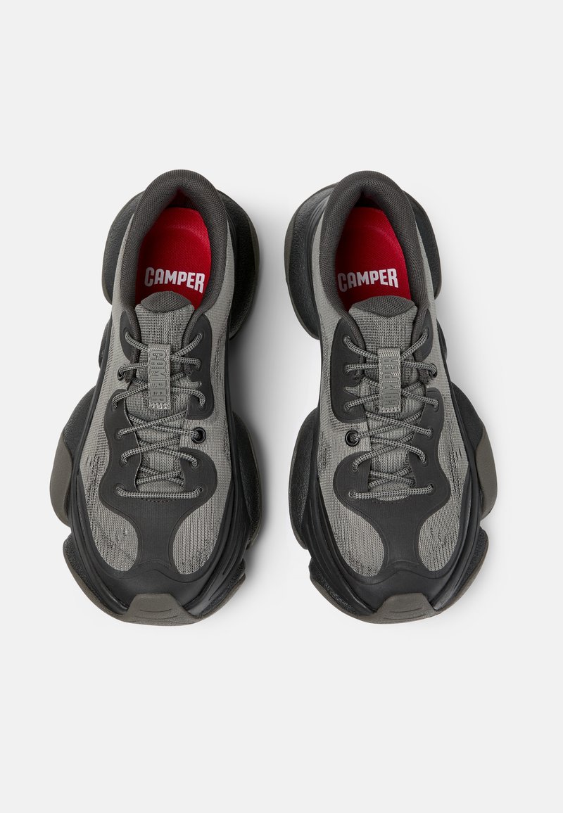 Graue Sportschuhe mit einem strukturierten Mesh-Obermaterial, gepolsterter Zunge, dicker schwarzer Gummisohle und rotem 'CAMPER'-Logo auf der Innensohle.