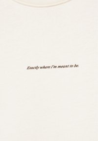 Tissu couleur crème avec texte italique marron centré indiquant "Exactly where I'm meant to be."