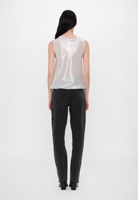 Haut sans manches en dentelle irisée avec un col rond, associé à un jean taille haute gris foncé et ajusté, et des talons épais noirs.