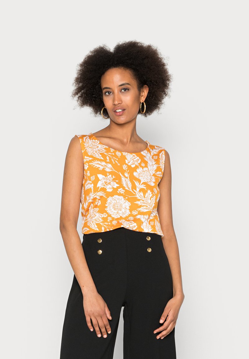 Top laranja sem mangas com padrão floral branco, decote redondo e detalhe frontal com nó, combinado com calças pretas de cintura alta com botões dourados.