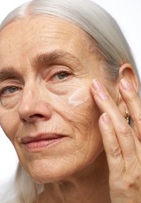 Fuktighetskräm applicerad på huden, genomskinlig lotion med krämig konsistens. Ämnet har ljust hår och synliga rynkor i ansiktet.