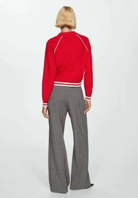 Rød cropped sweater med hvide vandrette striber ved kanten, parret med grå stribede vide bukser. Glat strikket tekstur synlig.