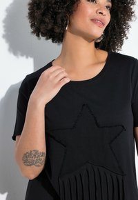 Sort t-shirt med en frynset stjerne-design på forsiden, med en glat tekstur og en rund halsudskæring. Korte ærmer kompletterer den afslappede stil.