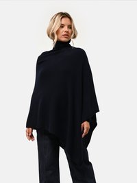 Poncho sovradimensionato blu navy con colletto alto, realizzato in un tessuto morbido e con un design drappeggiato. Abbinato a pantaloni in denim scuro.