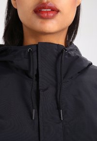 Black lightweight jacket features a drawstring hood, with sleek fabric and minimal detailing. The zipper and toggles are silver-toned.