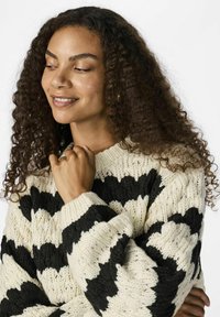 Gestrickter Pullover mit einer groben Textur, der ein schwarz-creamfarbenes wellenförmiges Muster, einen runden Kragen und gerippte Bündchen aufweist.