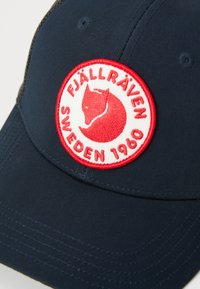 Marineblauwe pet met een rood-witte cirkelvormige Fjällräven logo patch met een gestileerd voshoofd en de tekst "Zweden 1960."
