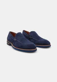 Navy modré semišové slip-on boty se švy, kulatou špičkou a koženou podšívkou. Obsahují hnědý kožený lem a kontrastní podrážku.