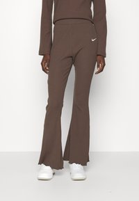 Bruna ribbade utsvängda byxor med midjeband, som har en vit Nike-logga. Tyget har en texturerad yta och en fransad nederkant.