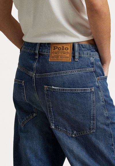 Denim jeans in dark blue with a textured finish. Features a brown leather patch labeled "Polo" on the back waistband, showcasing detailed stitching.