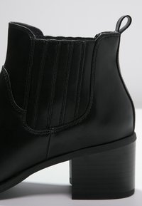Czarne botki sięgające kostki, wykonane ze skóry, z bocznymi elastycznymi panelami, okrągłym noskiem i blokowym obcasem. Posiadają gładką teksturę i minimalistyczne zdobienia.