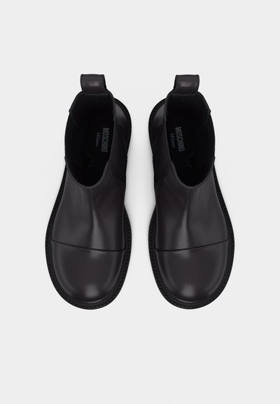 Ζευγάρι μαύρων δερμάτινων μποτών αστραγάλου με στρογγυλεμένες μύτες και θηλιές για τράβηγμα, από ψηλά, με την επωνυμία Moschino Milano στο εσωτερικό.