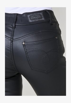 Tuvojums pie melnām ādas biksēm ar dekoratīvo šuvju rakstu uz aizmugurējā kabatas un Koroshi Denim Collection etiķeti uz jostas.