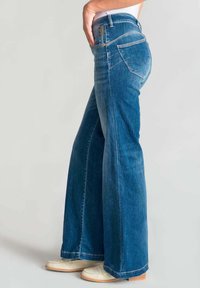 Jeans a zampa d'elefante in denim blu con vita alta, tasche laterali e cuciture a contrasto. Presentano un classico design a cinque tasche e una leggera scoloritura.
