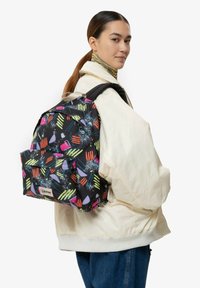 Černý batoh s barevnými abstraktními vzory, obsahující přední kapsu a ergonomické popruhy, vyrobený z odolné tkaniny.