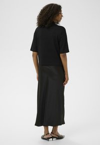 Zwart top met korte mouwen en lange, vloeiende zwart satijnen rok. De outfit heeft een losse pasvorm en een soepele textuur met minimale details.