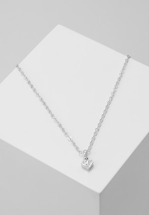 Delicate silver chain necklace with a small heart-shaped pendant featuring three clear gemstones, displayed on a white geometric block.