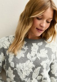 Jersey gris con un diseño floral en blanco, fabricado con un material suave. El escote es redondo, con un acabado texturizado y un ajuste relajado.