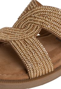 Sandalo con perline in tonalità dorate chiare, caratterizzato da un design incrociato, una soffice fodera in suede e una suola in gomma testurizzata.
