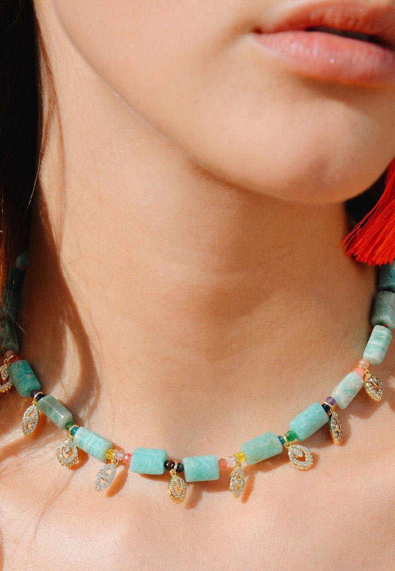 Collier en perles turquoises avec des pierres multicolores et des accents dorés. Présente des formes irrégulières et de petits pendentifs décoratifs.