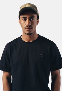 Černé bavlněné tričko s malou vyšitou fialovou slonem na hrudi. Doplněno khaki kšiltem s podobným logem slona.