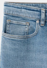 Poche de jean en denim bleu clair avec couture visible, rivet et passant de ceinture sur un fond uni.