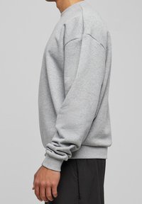 Sudadera gris con mangas largas, puños de canalé y cuello redondo. Confeccionada con una tela suave para mayor comodidad, presenta un corte holgado y una textura lisa.