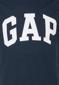 Navy blue cotton t-shirt featuring a bold white "GAP" logo in a stylized font across the chest. Smooth texture and casual fit.