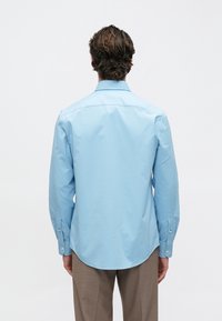 Chemise bleu clair à manches longues avec un col boutonné et un ourlet arrondi, fabriquée en tissu lisse. Présente des accents de poignets boutonnés.