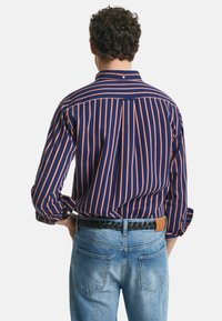Chemise à rayures bleu marine et orange avec un col classique, des manches longues et un détail d'empiècement, associée à un jean bleu clair et une ceinture tressée noire.