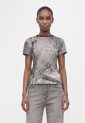 Femme portant un T-shirt gris ajusté avec un imprimé jean et un jean gris assorti, debout sur un fond blanc uni.