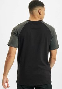 Svart og grå kortermet t-skjorte med raglan-design, glatt stofftekstur og rundt krage. Bakside viser kontrastfargede ermer.
