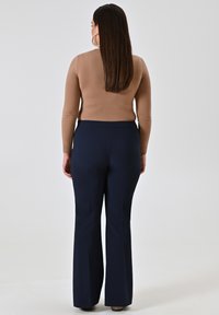Lichtbruin langekorte top gecombineerd met marineblauwe flared broek, met een soepele textuur en een aansluitende taille, gezien van achteren.
