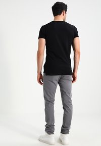 Černé tričko s krátkým rukávem a přiléhavým střihem, doplněné o šedé slim-fit kalhoty. Bílí tenisky dokončují celý outfit.