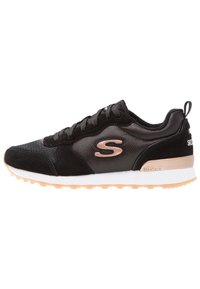 Schwarzer Sportschuh aus Mesh- und Wildledermaterialien, mit einem roségoldenen Logo, weißer Mittelsohle und strukturiertem Außensohle.