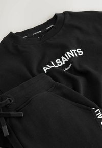 Schwarzes Sweatshirt und Jogginghose aus Baumwolle, mit weißem "ALLSAINTS LONDON" Logo. Der Stoff hat eine weiche Textur mit gerippten Bündchen und Kordelzügen.