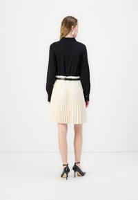 Chemise noire à manches longues avec col et détails de boutons, associée à une jupe plissée crème et des chaussures à talons noirs avec des brides de cheville.