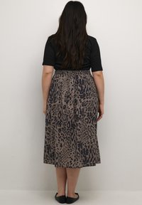 Maxirock mit einem Leopardenmuster in Beige und Schwarz. Hat einen elastischen Bund und eine fließende Silhouette. Kombiniert mit einem schwarzen Oberteil.