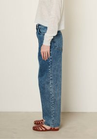 Hoggetaille lichte spijkerbroeken van denim met een rechte pijp, voorzien van klassieke vijf-pocket styling. Gecombineerd met platte bruine sandaaltjes.